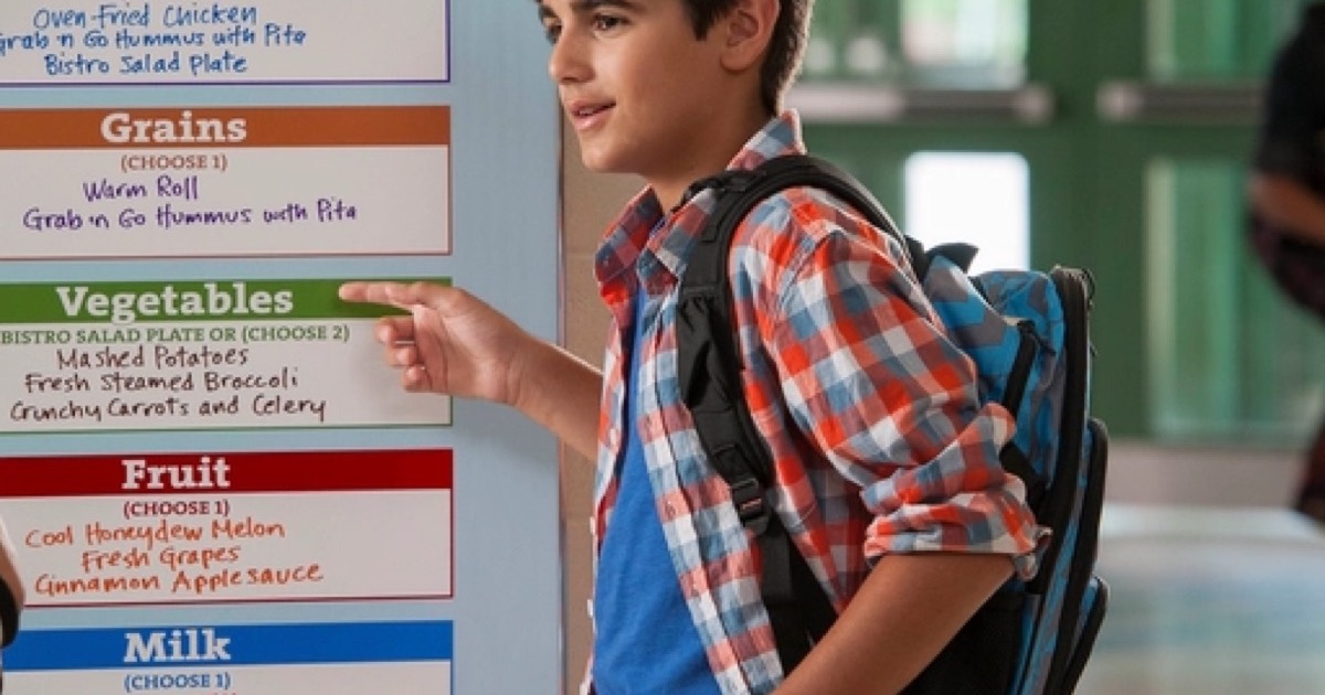 A preteen with a backpack reading a school cafeteria menu board