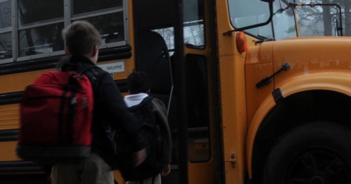 Two children with backpacks stepping onto a yellow school bus