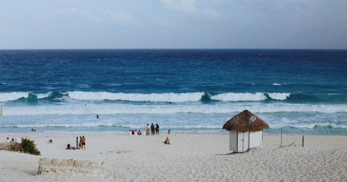 White sand beach with a thatched palapa hut and turquoise Caribbean waves under a blue sky