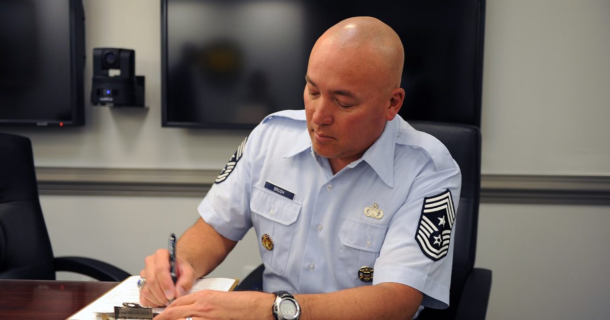Service member in uniform seated at a conference table filling out a vaccination form on a clipboard