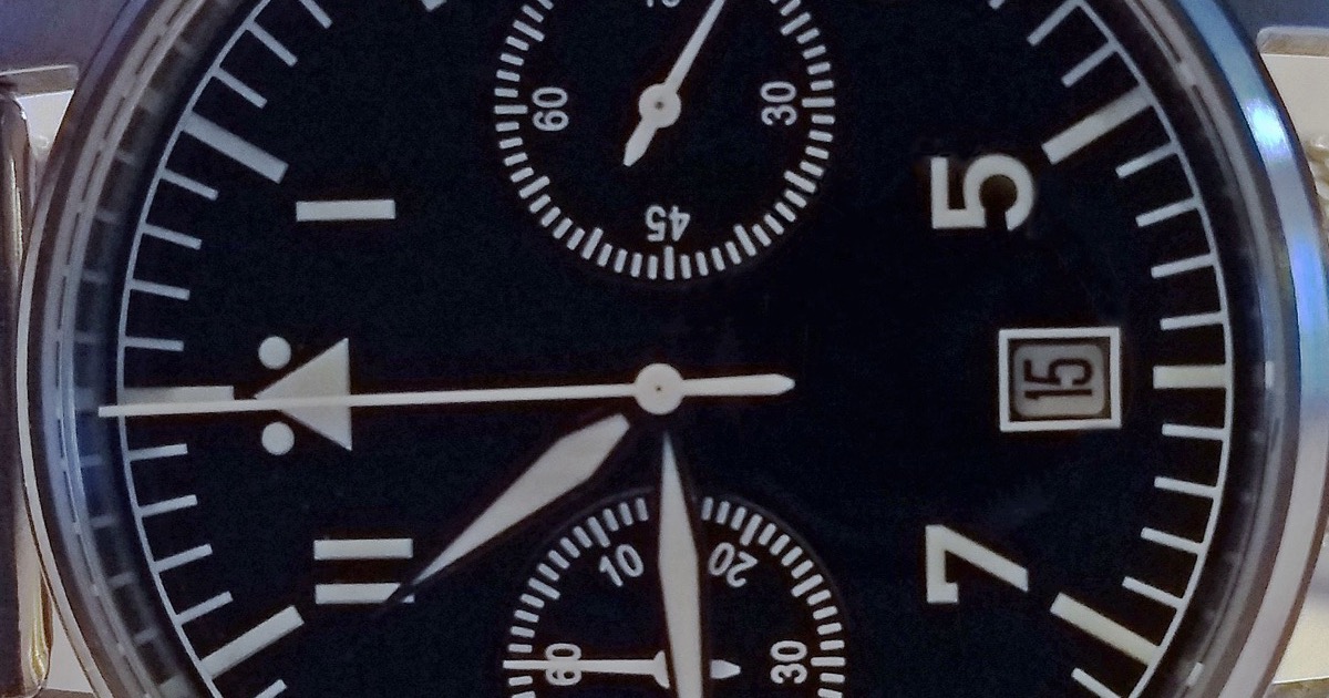 Close-up of a black chronograph watch dial with two subdials, a date window at 15 and luminous hands