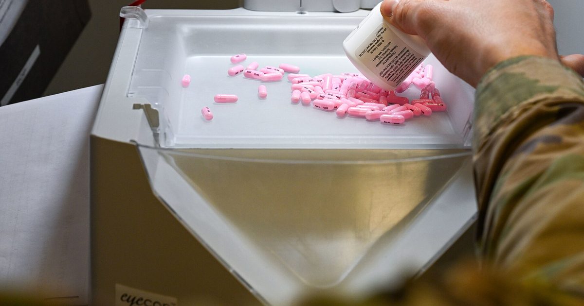 A pharmacy technician pours pink tablets from a bottle onto a white counting tray