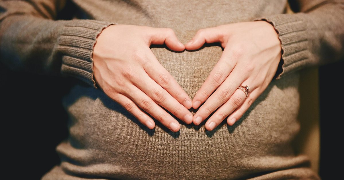 Pregnant woman in a knit sweater forming a heart with her hands over her belly