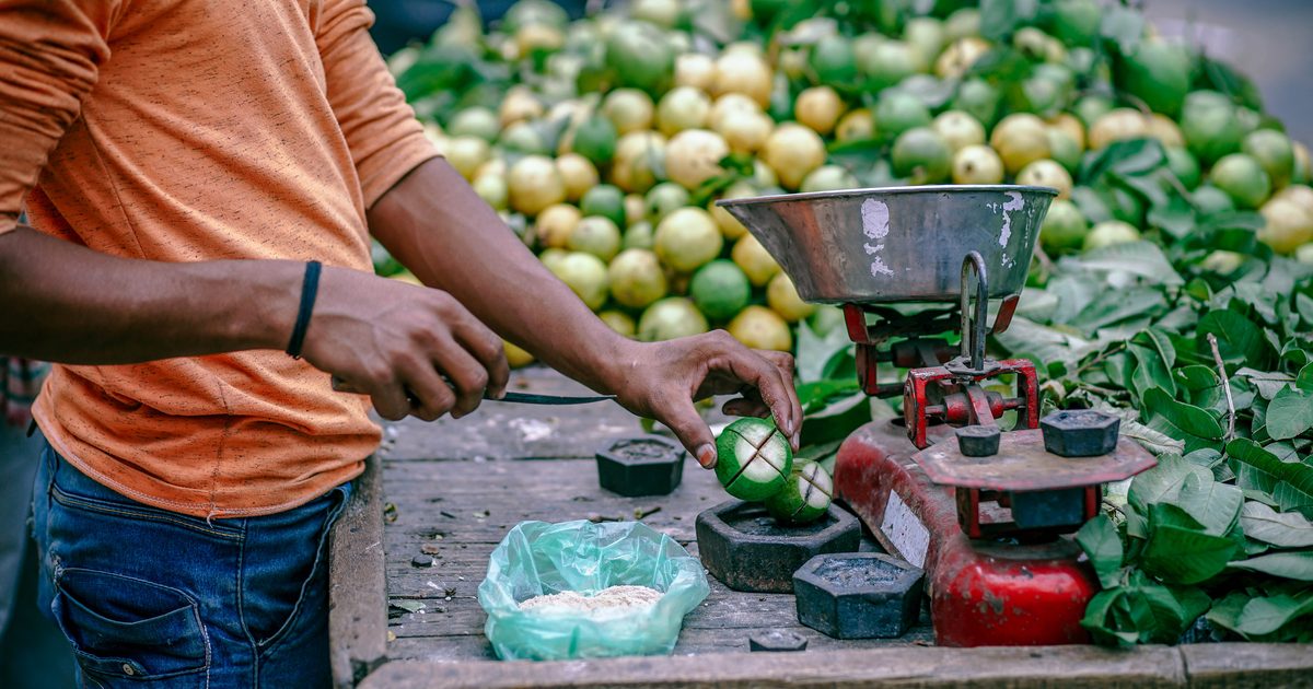 Street vendor weighing fresh produce on a hand scale at an outdoor market stall